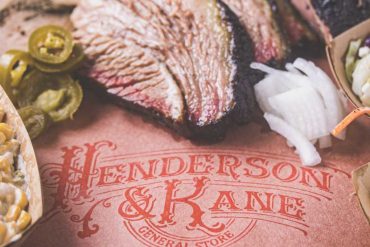 Juicy sliced smoked brisket with onions and jalapenos on a John Deere branded paper placemat, emphasizing American barbecue cuisine and food presentation.