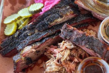 Smoked barbecue ribs with pickles, onions, and barbecue sauce, served on a tray, showcasing delicious American-style smoked meat dishes.