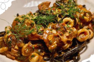 Spaghetti with seafood and herbs, served with a rich tomato sauce and garnished with fresh greens, ideal for travelers seeking authentic culinary experiences.