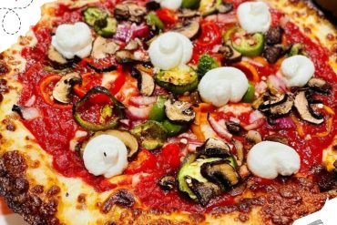 Fresh vegetable pizza topped with mushrooms, green peppers, red onions, and dollops of creamy cheese sauce. Perfect for a delicious meal from your favorite destination.