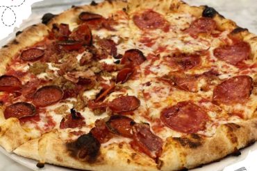 Savory pizza with pepperoni and sausage topping on a white plate.