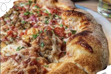 Crispy stuffed pizza with melted cheese, fresh herbs, and savory toppings on a wooden table for authentic Italian pizza experience.