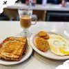 Toasted bread with fried eggs and hash browns, along with a glass of coffee, served as a delicious breakfast at a local café. Perfect for travelers seeking a hearty meal during their adventures.