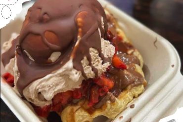 Rich chocolate ice cream sundae topped with strawberries and whipped cream served in a disposable container. Perfect for desserts and sweet treats in travel destinations.