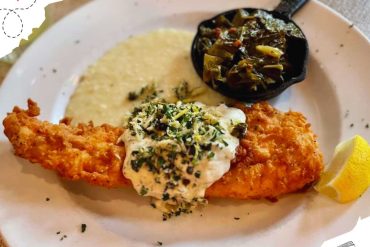Crispy fried fish fillet with coleslaw, mashed plantains, and a side of sautéed greens served on a white plate for authentic Caribbean cuisine.