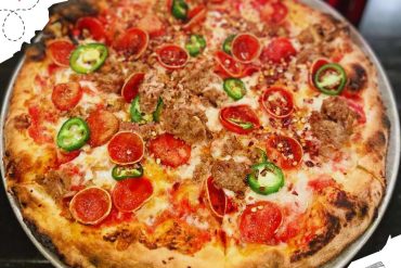 Hot and delicious pepperoni sausage pizza topped with sliced jalapenos and red chili flakes, served on a silver tray, perfect for travel and food lovers exploring renowned destinations worldwide.