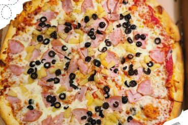Freshly baked pizza topped with ham, pineapple, black olives, and cheese, showcasing delicious international cuisine for travel and dining enthusiasts.