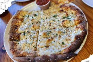 Cheese and garlic pizza with side of marinara sauce on white plate.