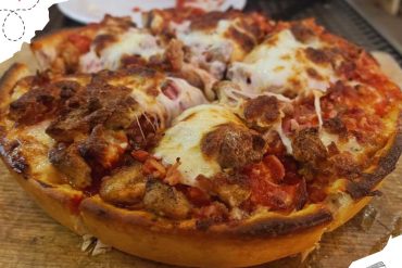 Cheesy meat lover's pizza with sausage, ground beef, tomato sauce, melted cheese, and crispy crust, perfect for Italian cuisine and pizza delivery.
