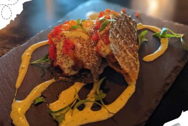 Crispy fried fish tacos with spicy aioli and fresh herbs on a wooden serving board, served as a delicious dish at a travel-themed restaurant, perfect for food lovers and travel enthusiasts alike.