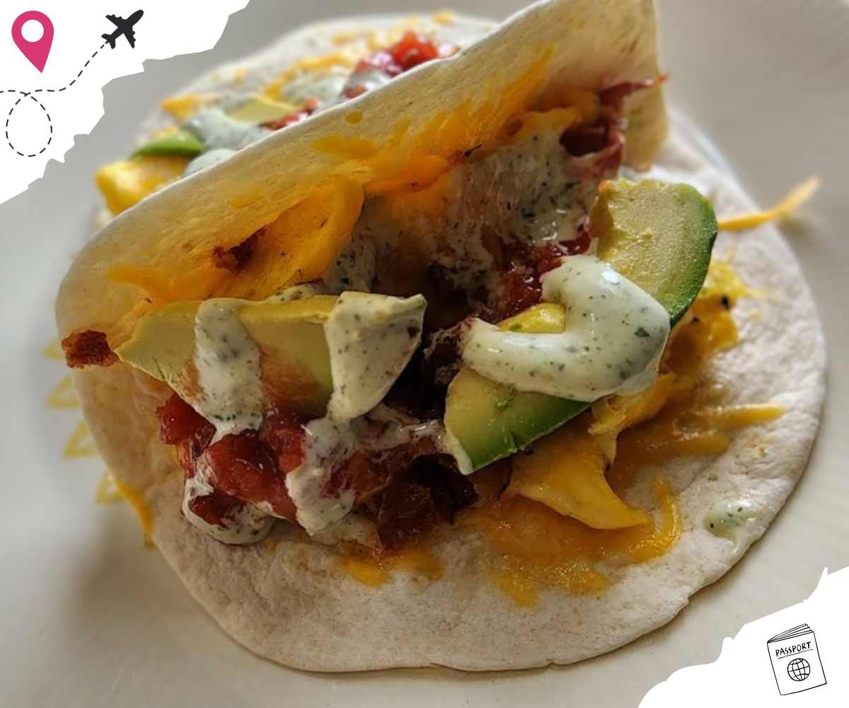 Savory breakfast taco with scrambled eggs, avocado, bacon, and creamy sauce on a soft tortilla, perfect for travel destinations and food adventures.