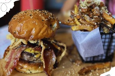 Juicy gourmet burger with crispy bacon and fried onion topping served alongside seasoned French fries topped with cheese and gravy, perfect for comfort food lovers.
