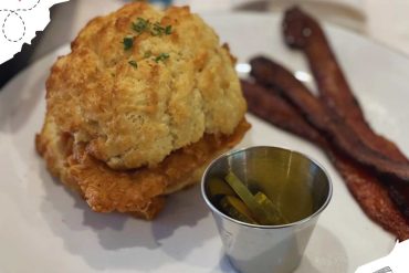 Crispy fried chicken and bacon strips with dipping sauce on white plate.