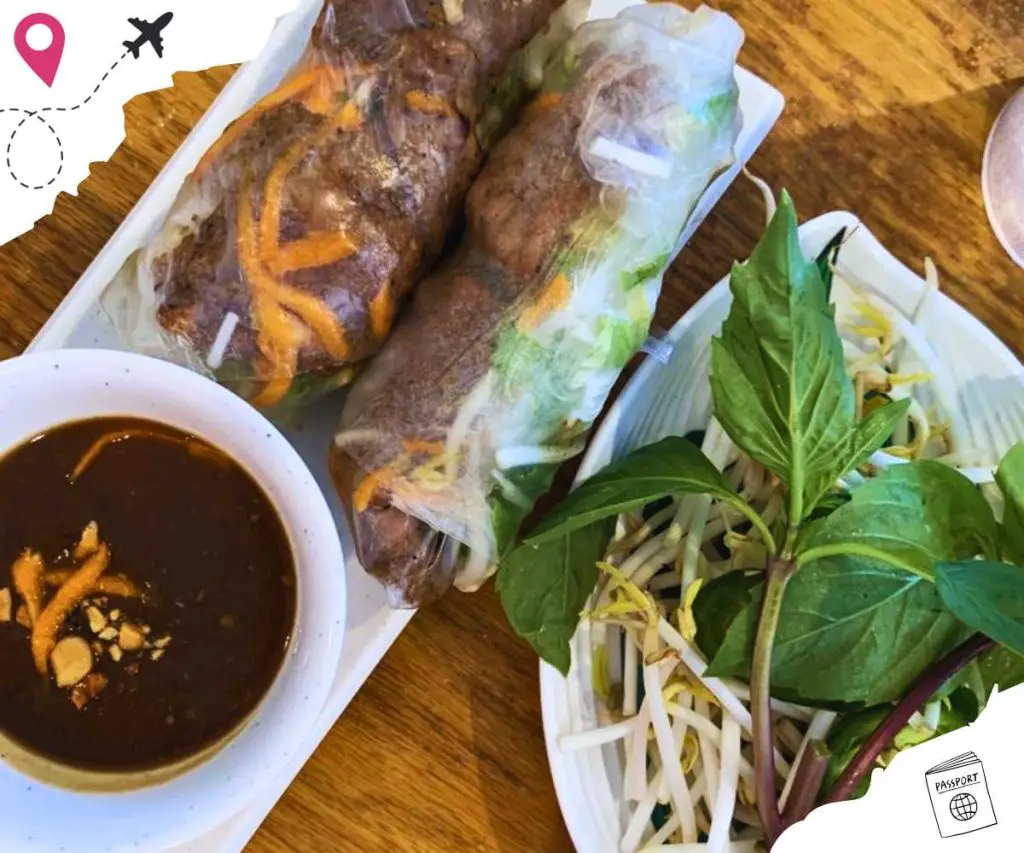 Grilled pork spring rolls with a bowl of sauce and a plate of fresh garnishes.