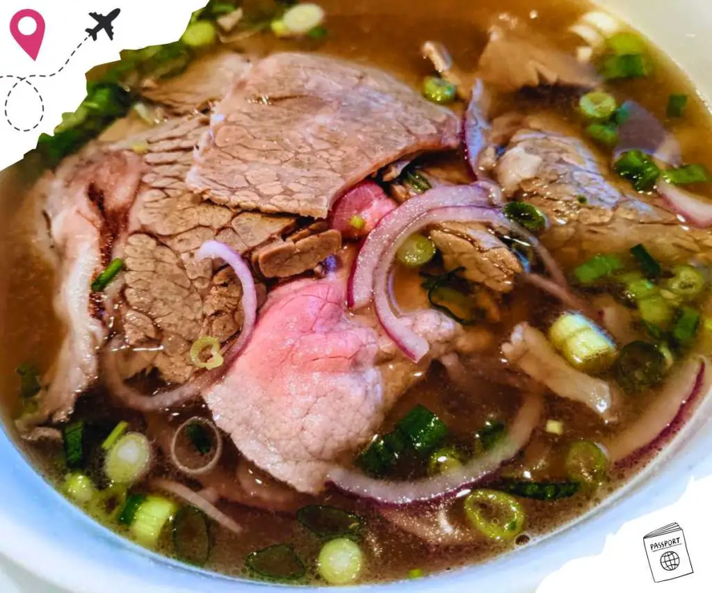 A close up of a bowl of pho, with slices of meat, red onions, and scallions.