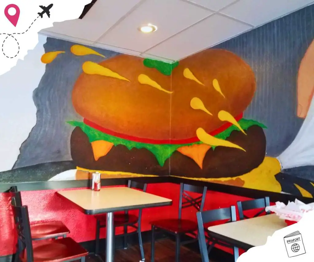 Tables and chairs in front of a decorated corner; a large cheeseburger is painted on the wall.