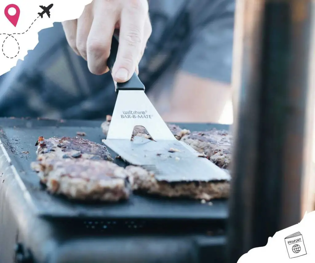 A spatula being used to press beef patties onto the grill.