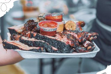 Juicy smoked ribs with BBQ sauce and dipping sauces served on a disposable plate, perfect for a Texas BBQ experience.
