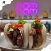 Beef bao bun dishes with fresh herbs and chili toppings at a restaurant in front of decorative neon sign, Asian cuisine, street food, gourmet food, trendy dining atmosphere.