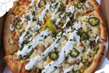 Crispy chicken pizza with jalapeños, corn, and cilantro topped with creamy sauce and lime wedge, fresh hot pizza from a restaurant, delicious comfort food, popular dish for travel and food lovers.