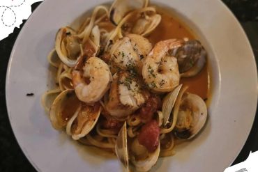 Seafood pasta with shrimp, clams, and tomato sauce garnished with herbs, served on a white plate for an authentic Italian dining experience.
