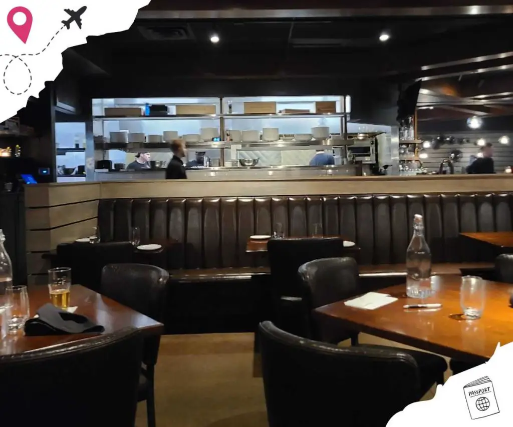 Modern restaurant interior with open kitchen, dark wood furniture, and dim lighting, perfect for dining and travel enjoyment.