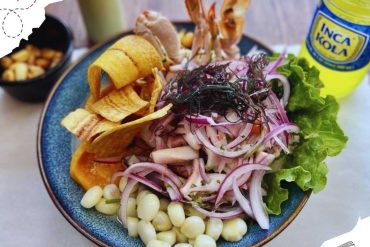 Fresh Peruvian ceviche with onions, corn, sweet potato, and lettuce, served in a vibrant blue bowl, accompanied by inca kola soda, showcasing authentic South American cuisine.