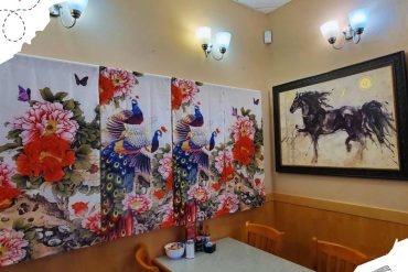 Peacock and floral wall art in a cozy restaurant interior, colorful and vibrant decor with artwork of horses, perfect for travel and destination-themed dining experiences.