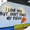 Enjoyable pizza restaurant wall art with humorous quote about love and pizza, featuring colorful pizza illustration, bright interior decor, and modern design elements, perfect for travel and food lovers.