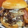 Crispy bacon cheeseburger with caramelized onions and melted cheese on a soft sandwich bun, served with seasoned fries, perfect for comfort food lovers seeking flavorful travel food adventures.