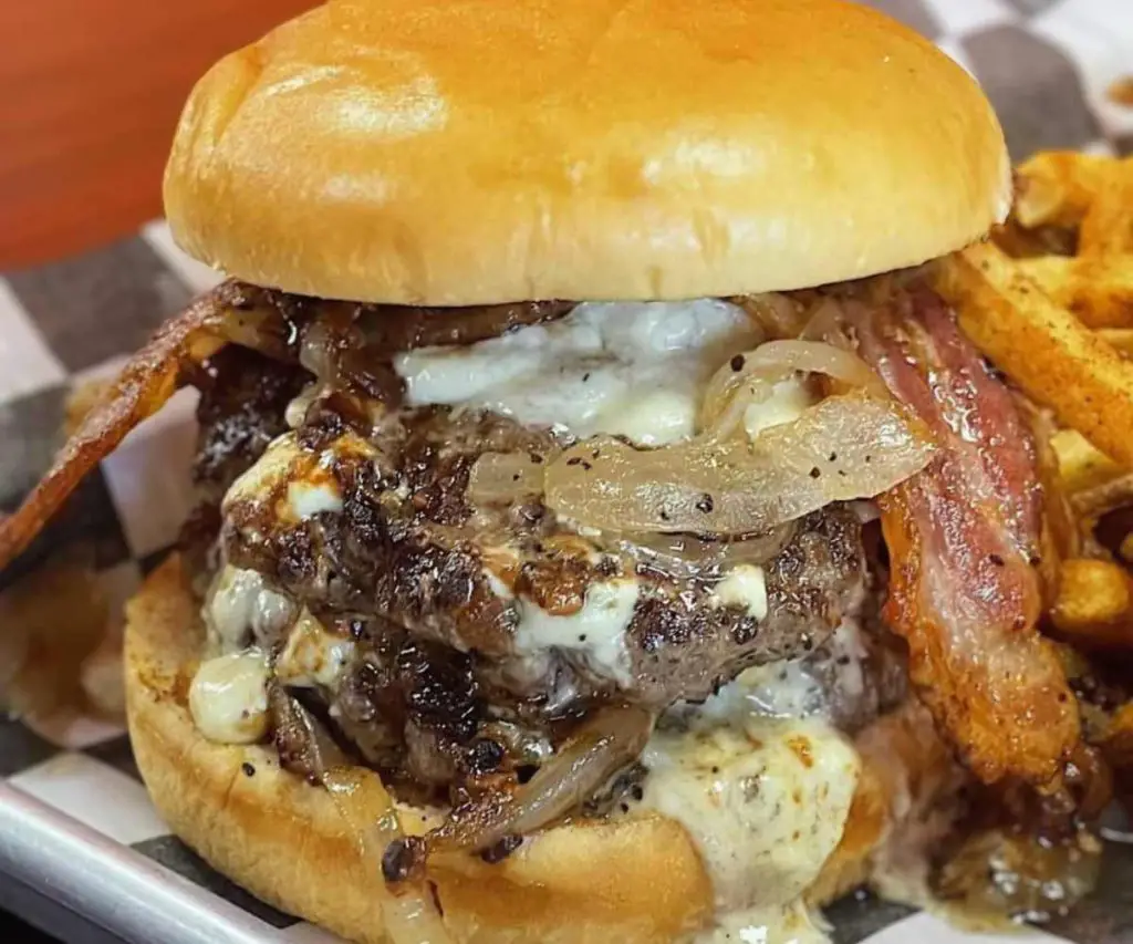 Crispy bacon cheeseburger with caramelized onions and melted cheese on a soft sandwich bun, served with seasoned fries, perfect for comfort food lovers seeking flavorful travel food adventures.