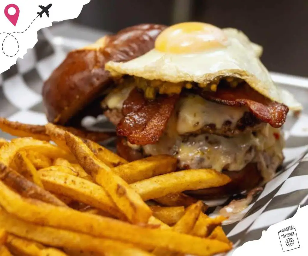 Cheeseburger with bacon and fries, gourmet burger, American comfort food, juicy beef patty, crispy bacon, fried egg, golden French fries, fast food, casual dining, indulgent meal, restaurant cuisine, delicious burger meal.