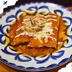 Two enchiladas topped with cheese and garnish on a blue and white decorated plate.