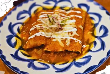 Two enchiladas topped with cheese and garnish on a blue and white decorated plate.