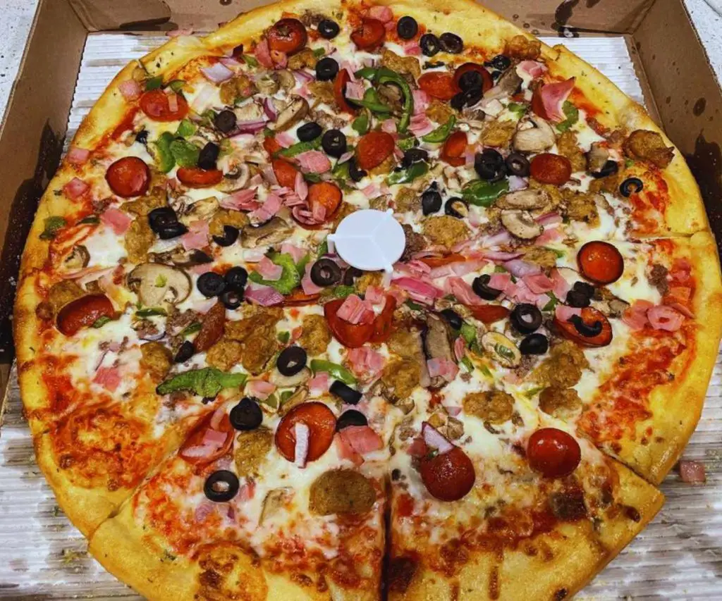 Flatbread pizza with various toppings including cherry tomatoes, mushrooms, green bell peppers, black olives, and ham on a golden crust.