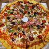 Crispy pizza with pepperoni, sausage, olives, mushrooms, green peppers, and ham in a takeout box.