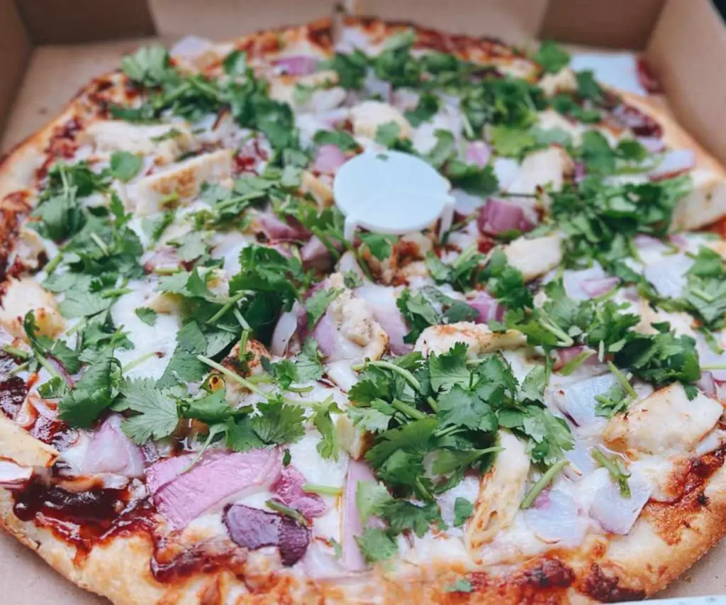 Delicious pizza topped with fresh cilantro, onions, and shredded chicken in a pizza box for takeout or delivery.