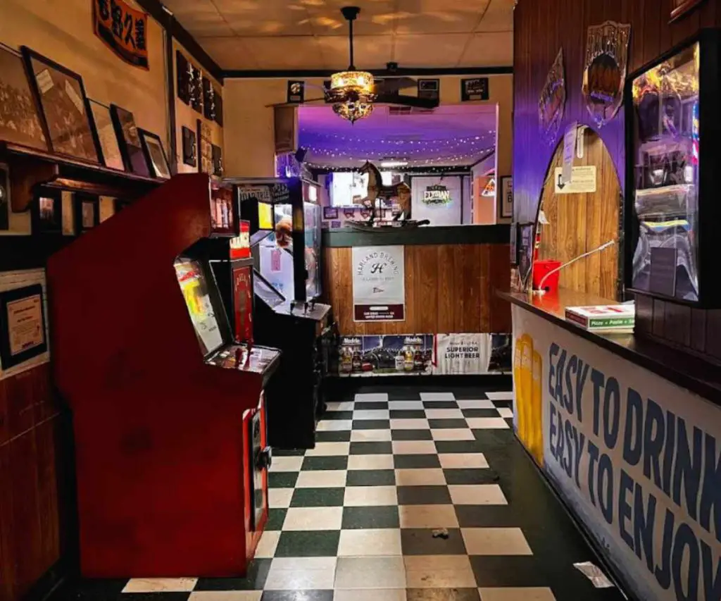 Vintage arcade game machines inside a cozy bar with checkered flooring and warm lighting, creating a nostalgic and inviting atmosphere for entertainment and nightlife.