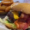 Juicy bacon cheeseburger with grilled beef patty, melted cheddar cheese, crispy bacon, fresh lettuce, and tomato served with crispy onion rings on the side. Perfect for classic American fast food lovers.