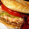 Moist burger with lettuce, tomato, bacon, and sesame seed bun, served with creamy sauce, close-up gourmet fast food image.