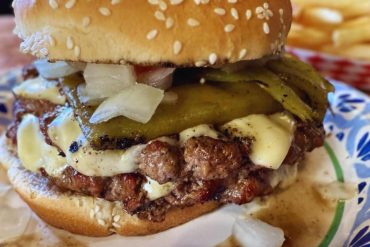 Juicy cheeseburger with pickles and onions on a sesame seed bun, served with fries in the background, highlighting classic American comfort food, perfect for travel and culinary adventures.