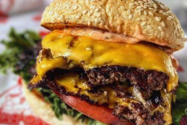 Juicy cheeseburger with sesame seed bun, melted cheddar, crisp lettuce, ripe tomato, and savory beef patty on a bed of greens, close-up of delicious American-style fast food.