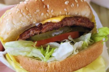 Fresh cheeseburger with lettuce, tomato, pickles, and sesame seed bun, showcasing delicious fast food comfort, perfect for travel food stops and local cuisine experiences.