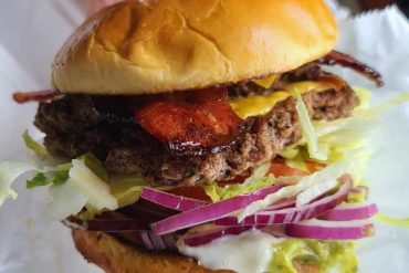 Juicy cheeseburger with crispy bacon, fresh vegetables, and melted cheese, served in a soft bun, perfect for food lovers, ideal for travel and dining experiences at top destinations worldwide.