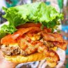 Freshly prepared gourmet burger with lettuce, tomato, crispy bacon, and melted cheese, served in a soft bun. Perfect for a tasty outdoor meal and travel food adventures.