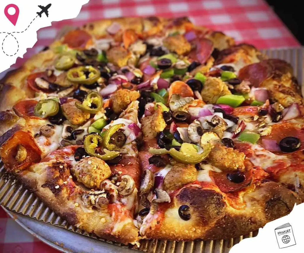 Delicious loaded pizza with olives, pepperoni, sausage, peppers, and onions on a crispy crust in a takeout box.