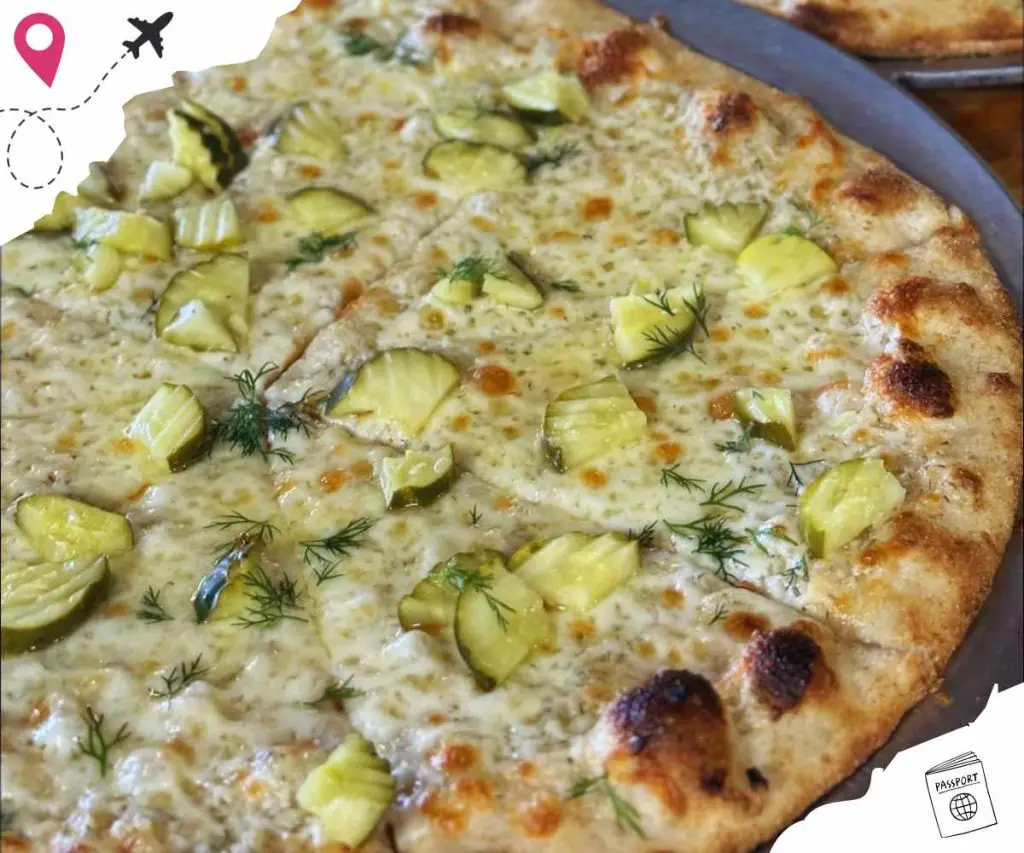 Sauced pizza with pickles garnished with dill on a dark plate, close-up shot.
