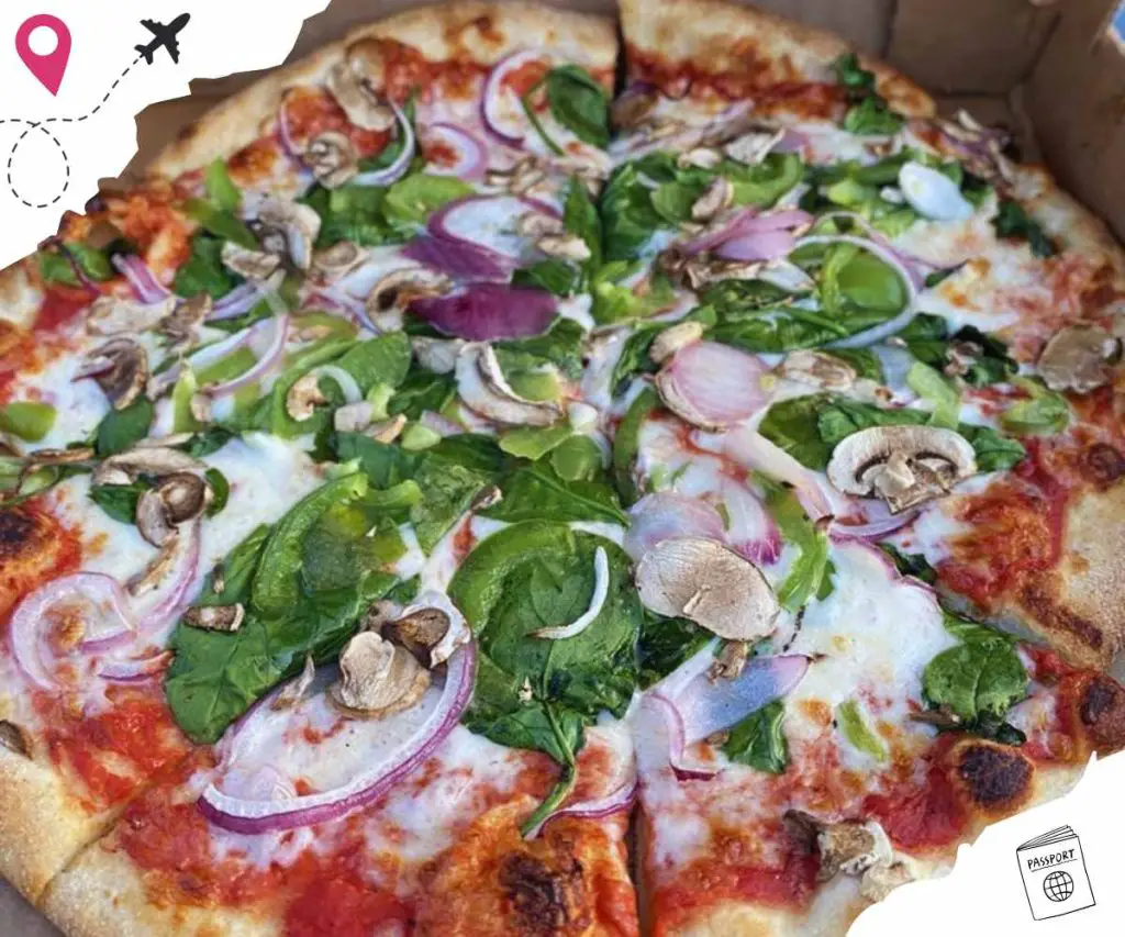 Fresh vegetable pizza with spinach, mushrooms, red onions, and tomato sauce, perfect for travel food lovers. Ideal for those seeking delicious pizza options while exploring new destinations.