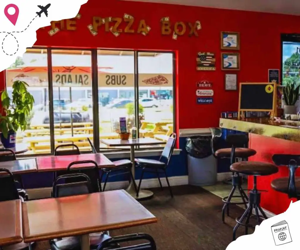 Comfortable pizza restaurant interior with colorful decor, featuring tables and chairs, and a view of the outdoor seating area through glass doors. Perfect for enjoying pizza in a cozy setting.