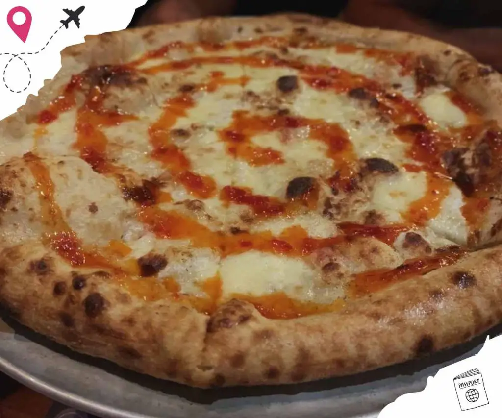 Cheese pizza with a golden-brown crust, melted cheese, and drizzled hot sauce, served on a plate. Ideal for pizza lovers seeking authentic Italian flavors and popular travel cuisine.